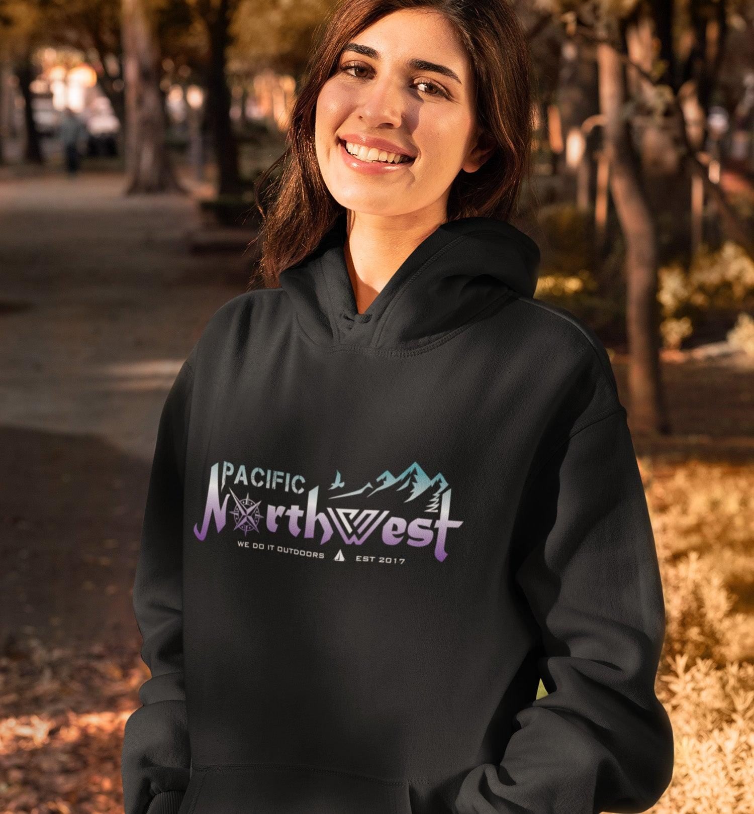 Person wearing a black hoodie with 'Pacific Northwest' text and mountain design outdoors.