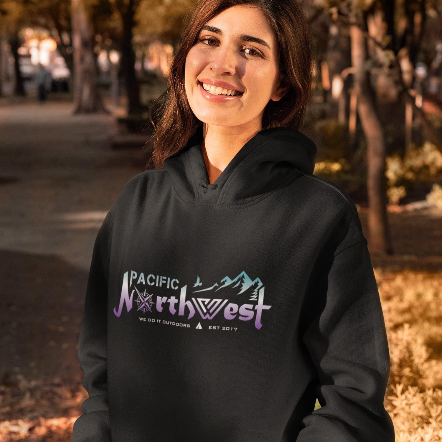 Person wearing a black hoodie with 'Pacific Northwest' text and mountain design outdoors.