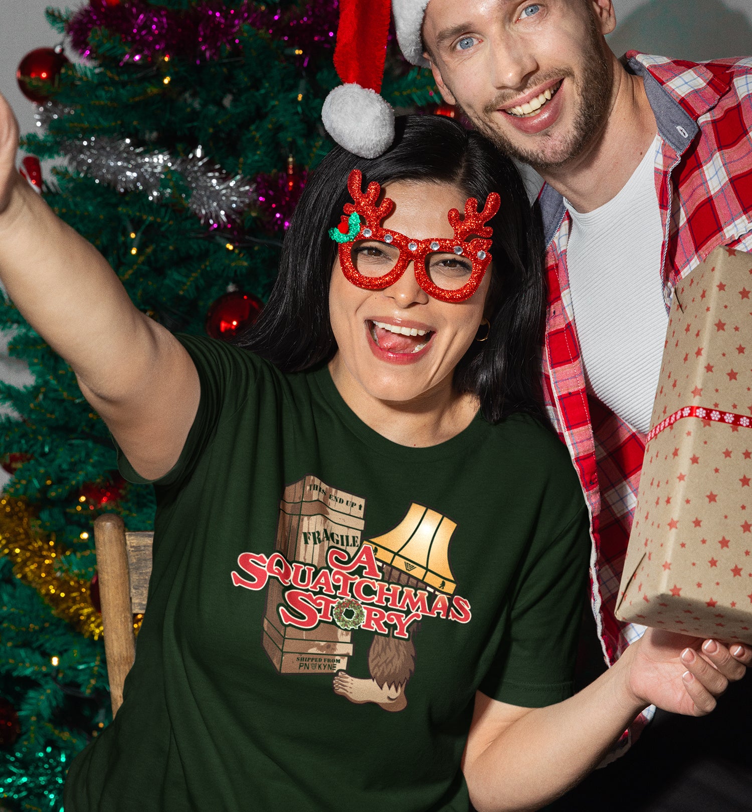 A Squatchmas Story Bigfoot shirt on a woman by a Christmas tree