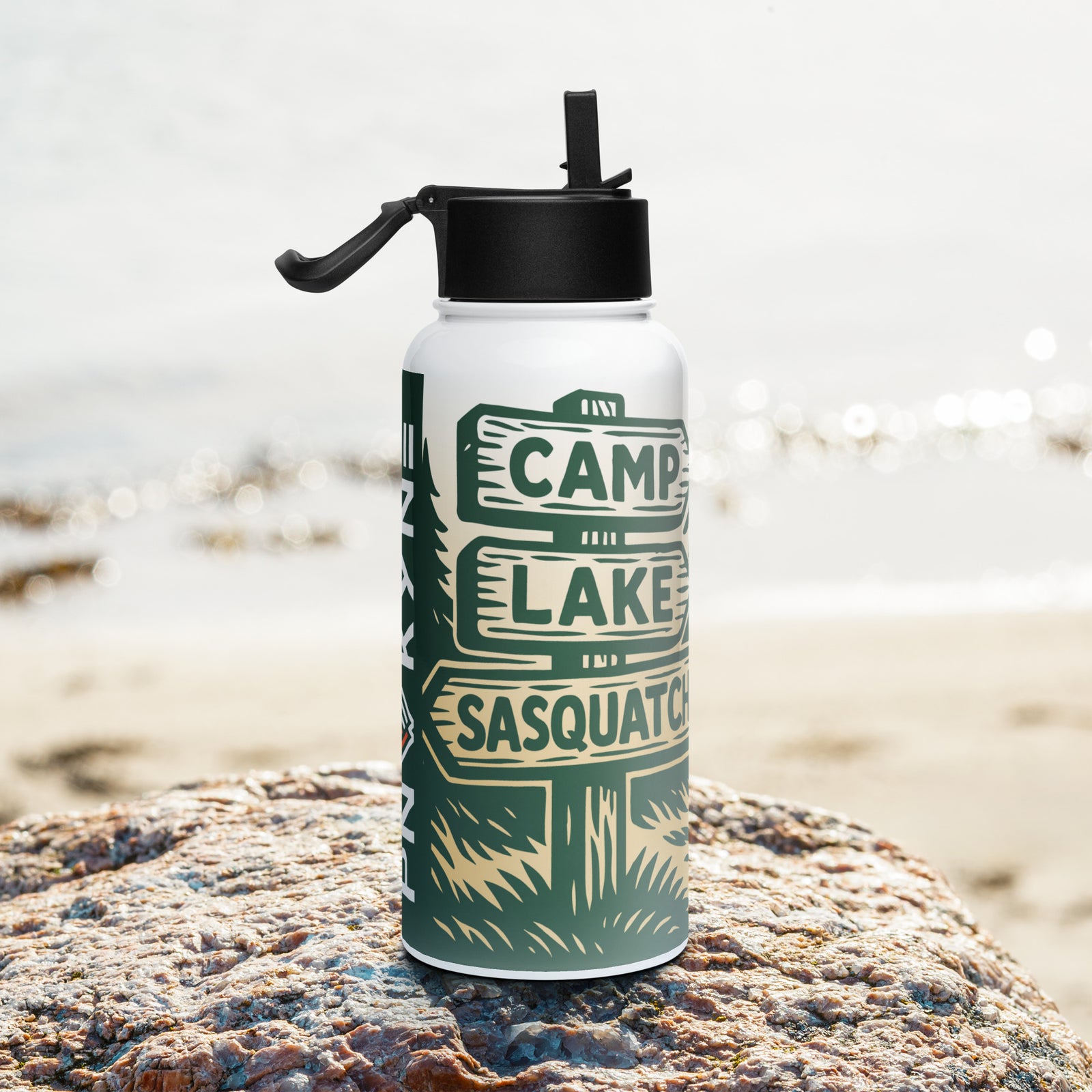 Water bottle with Bigfoot camping-themed design featuring a sign post pointing towards Camp, Lake, and Sasquatch, on a rock by the beach.