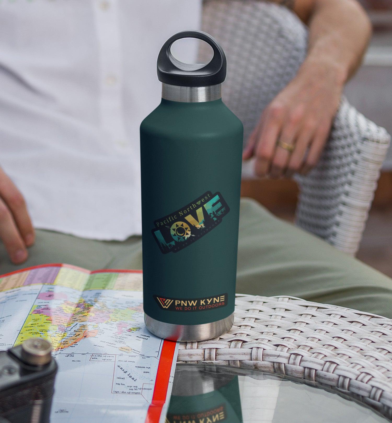 Green water bottle featuring a Pacific Northwest LOVE sticker and PNW Kyne sticker on a table next to a map and camera