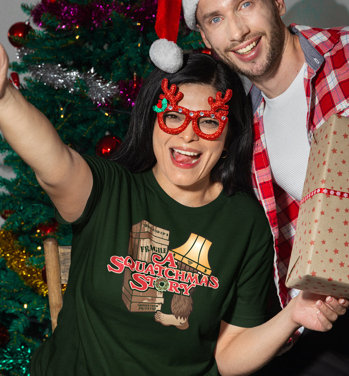 A Squatchmas Story Bigfoot shirt on a woman by a Christmas tree