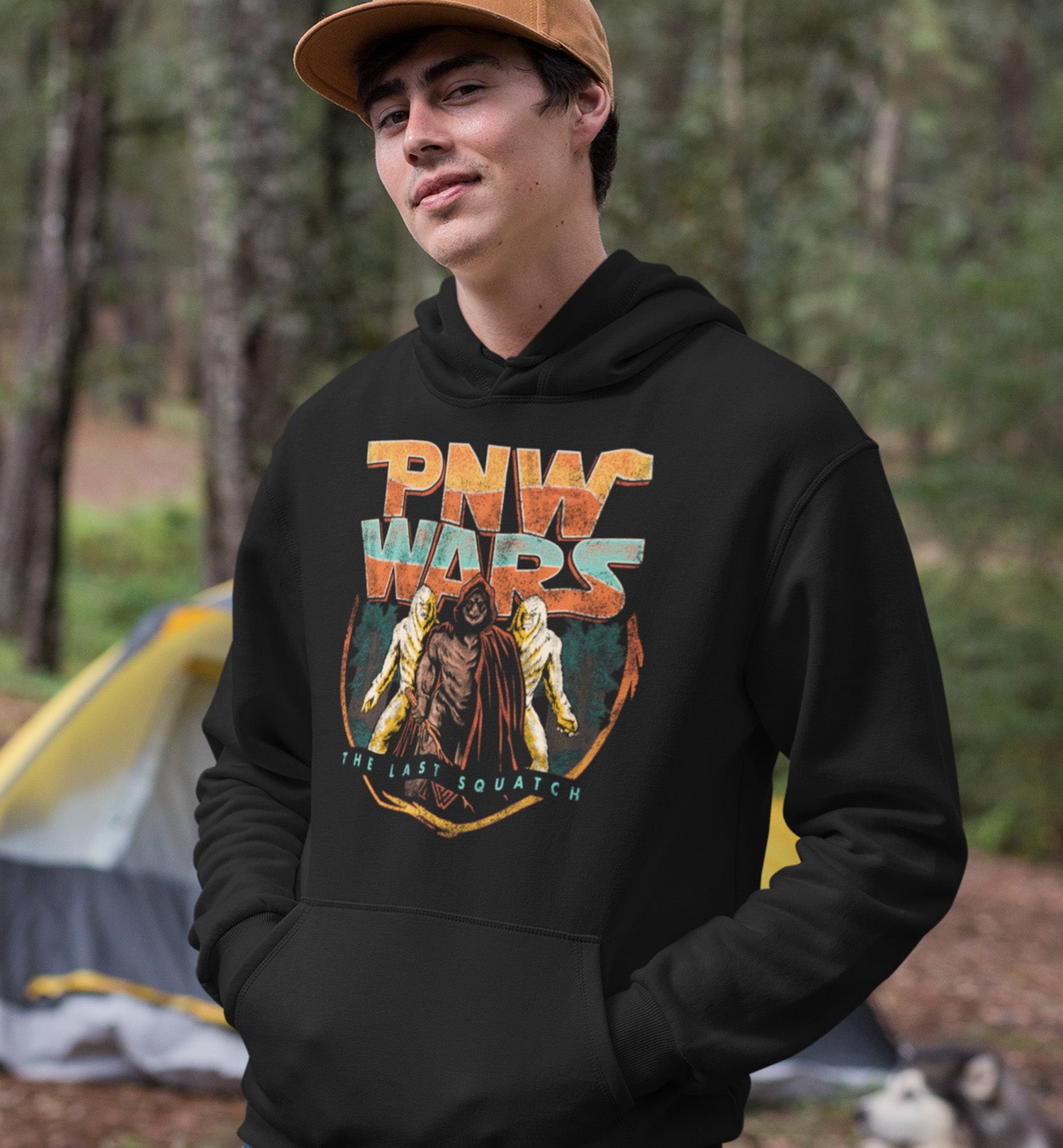 Man wearing a PNW Wars Last Squatch hoodie at a camp site